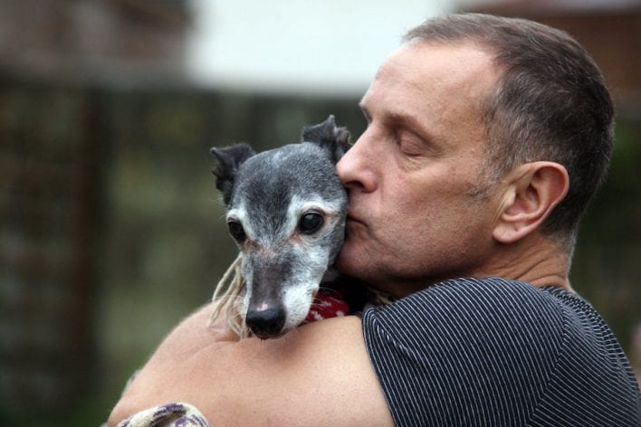 Mark Woods kisses his dog Walnut before taking him to Porth beach for a final walk, November 12 2016. See SWNS story SWWALNUT; Hundreds of animal lovers turned out yesterday (at) to support a heartbroken dog owner as he took his beloved pet on its final walk. Mark Woods stole the nation's heart after he appealed for fellow dog lovers to join him on his last walk with Walnut, the 18-year-old whippet he has has had since a puppy. Hordes of well-wishers, many accompanied by their own dogs, joined Mark and his family on a wind swept Porth beach, Newquay in Cornwall for Walnut's emotional farewell. Mark carried Walnut across the beach as his health has deteriorated in old age and he's no longer able to walk.